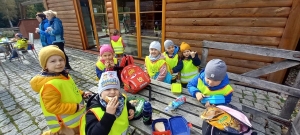 Dzieci w kurtkach i w 
czapkach siedzą przy 
drewnianym stole.