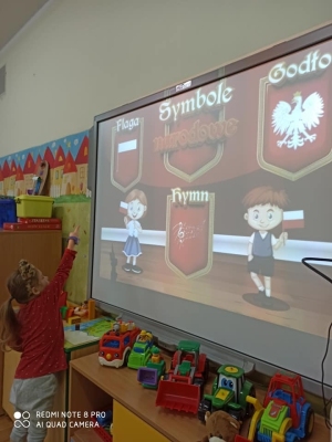Dziewczynka wskazuje flagę Polski na prezentacji.