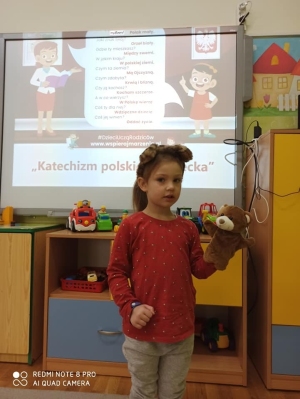 Dziewczynka z Misiem Pysiem mówi z pomocą nauczyciela "Katechizm polskiego dziecka".